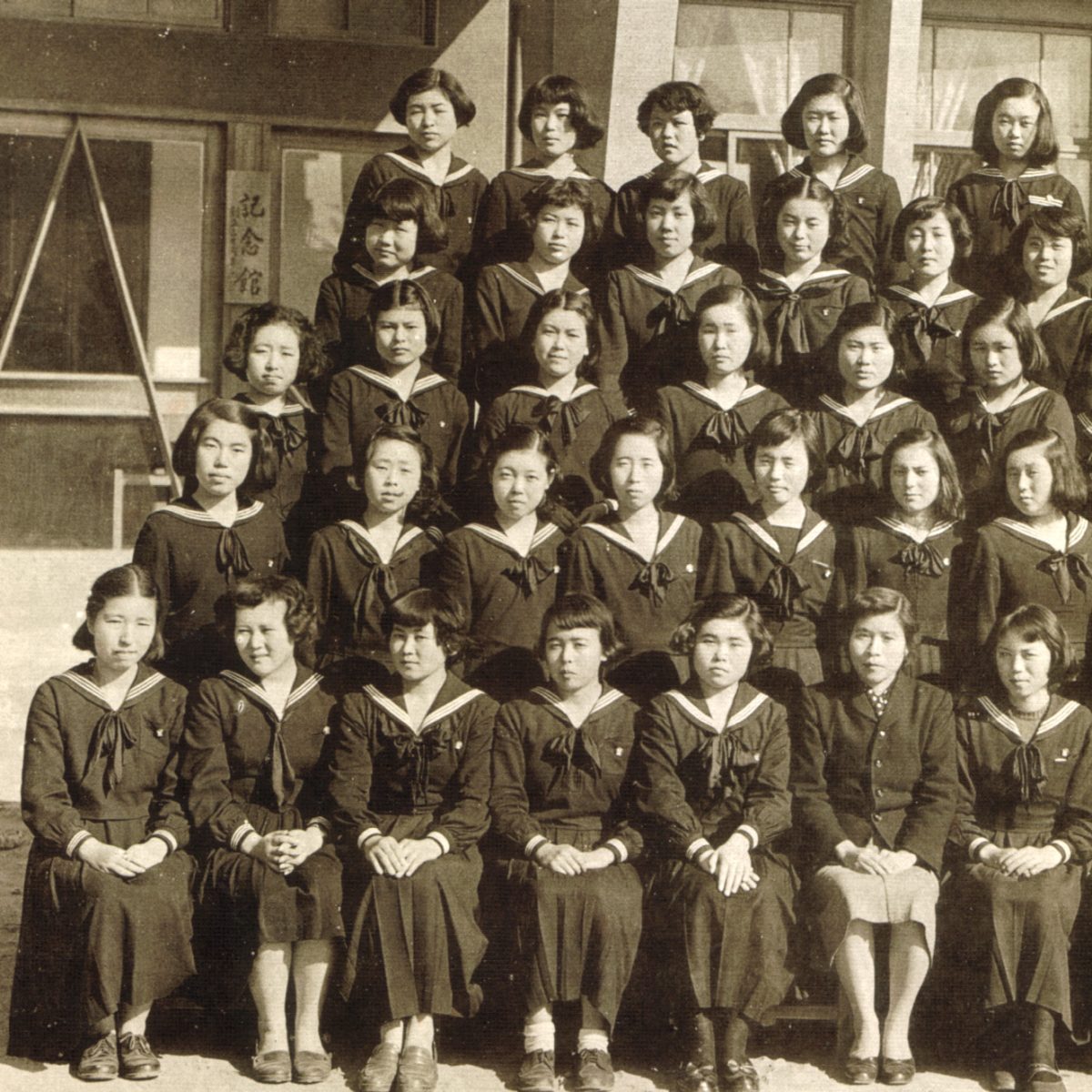 1955(昭和30)年の集合写真<br />
奥に、この年に創立30周年記念事業として<br />
竣工された、音楽、図書室、普通教室を擁する持つ<br />
記念館がある